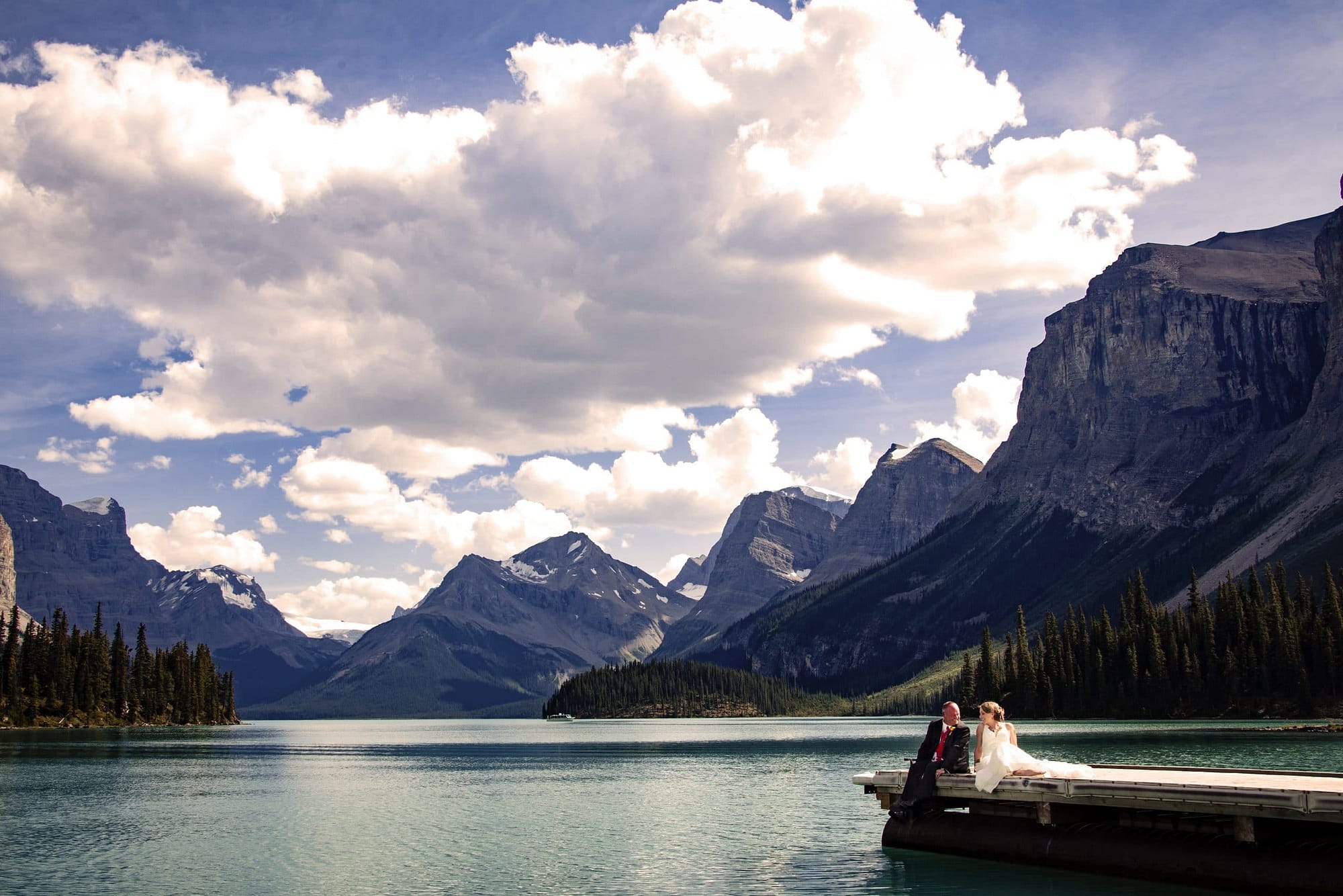 wedding couple sitting on a dock at Maligne Lake - Your Jasper wedding photography consultation