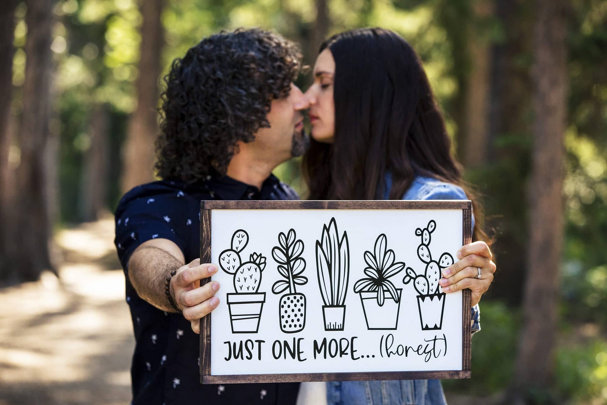 couple kissing while holding up a sign announcing pregnancy- family photos in Jasper