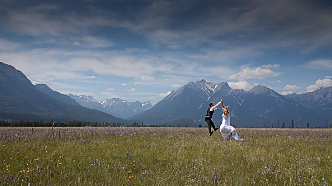 Bride and groom jumping up and high-fiving with mountain valley in the background