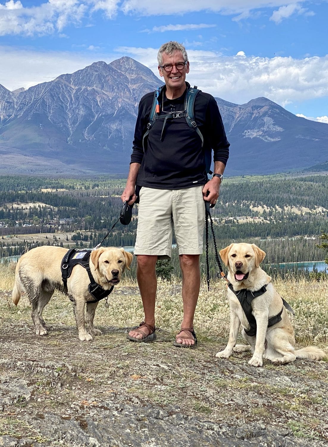 man standing in front of Pyramid Mountain with two yellow labs