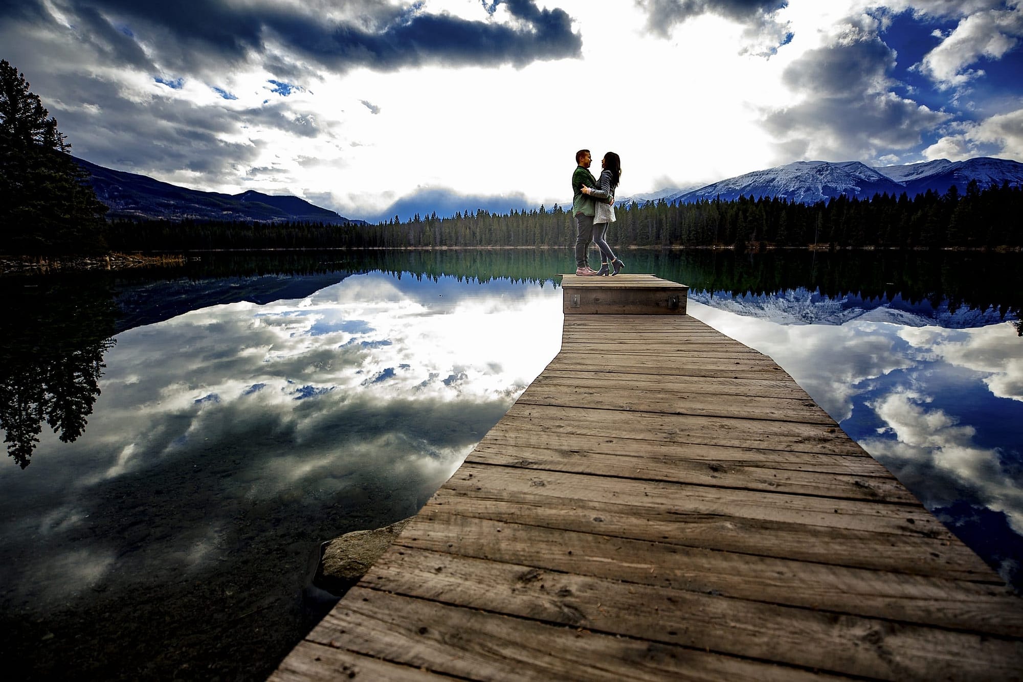 man and woman silhouetted on the sky at the end of the dock at Lake Edith | Jasper engagement photographers