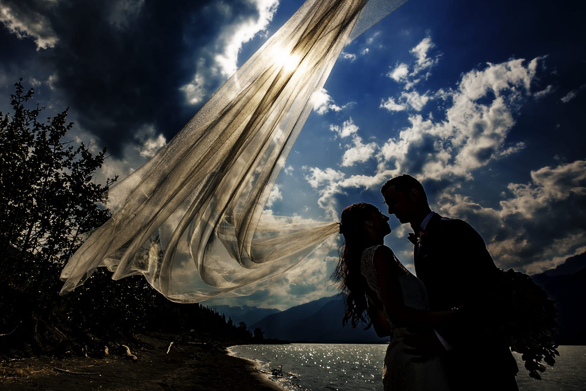 Silhouette of wedding couple against clouds and blue sky- Jasper Lake Wedding Photos